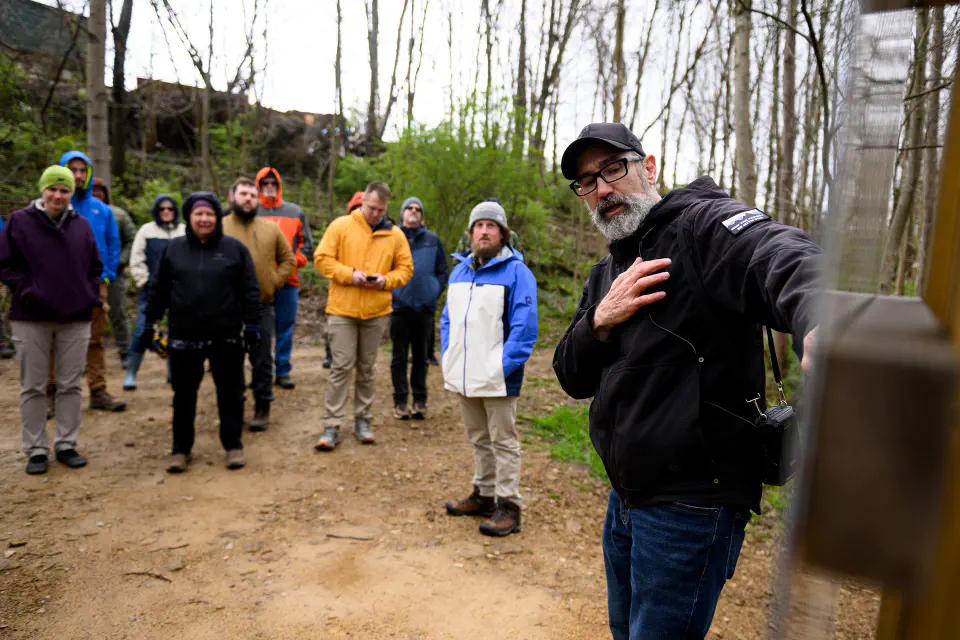 A man explaining trail signage to a big group standing in a circle in the woods