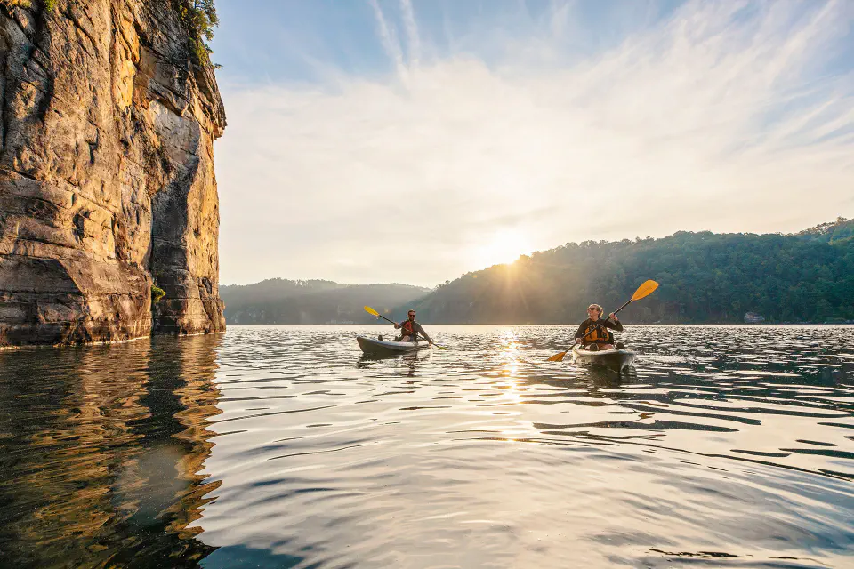 Two people kayaking on a lake next to a cliff face