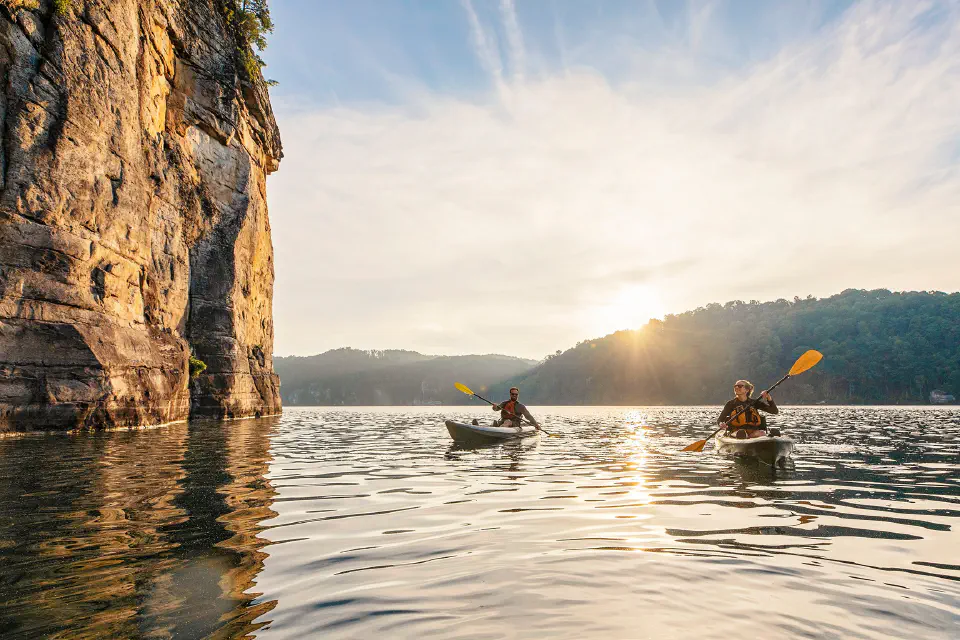 Two kayakers on a lake next to a cliff face
