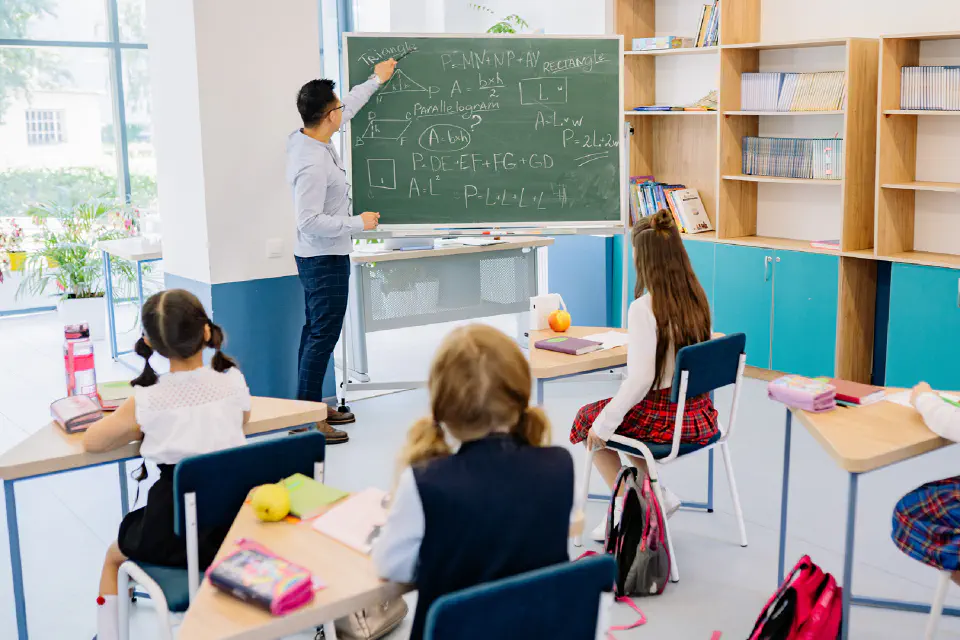 A teacher at a blackboard in front of a class of childeren