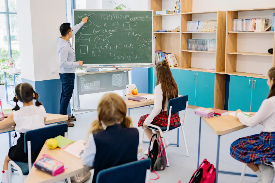 A teacher at a blackboard in front of a class of young stu