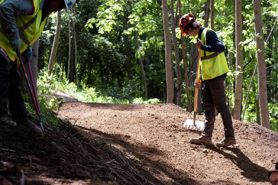 Two trail workers wearing safety equipment digging a trail