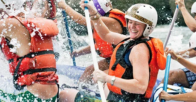 Close up shot of a young woman smiling while getting splashed by a wave in a raft on the New River Gorge.