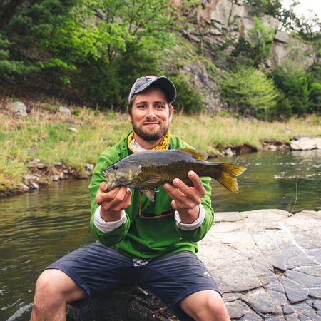 Travis Hines holding a fish he caught next to a river