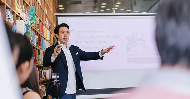 An asian man gives a presentation in front of a small crowd.