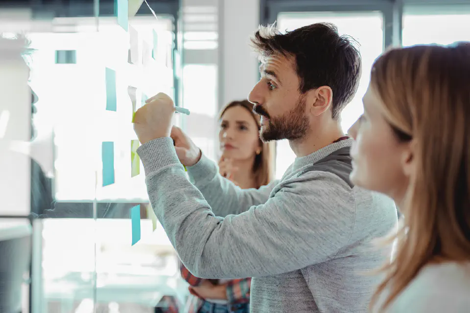 Three people writing on sticky notes at a white board